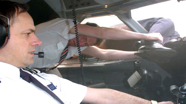 a man in a white shirt and tie holding his head in the cockpit of a plane